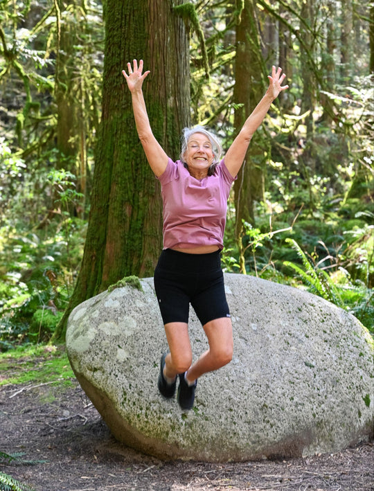 Person jumping in front of large rock in a forest