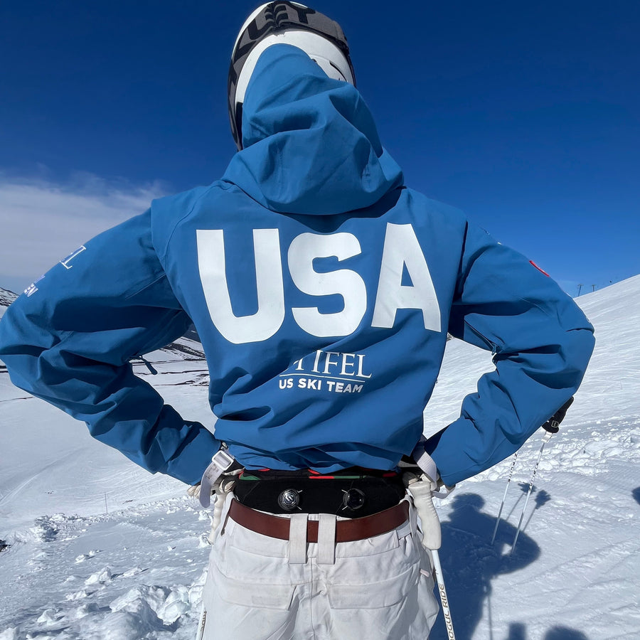 Person in a blue jacket with 'USA' on it, standing on a snowy landscape.